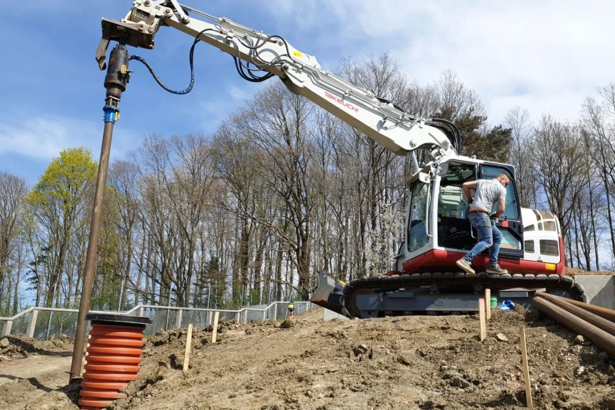 Graafmachine met hydraulische schroefmotor plaatst schroefpalen op een werf van Soiltek