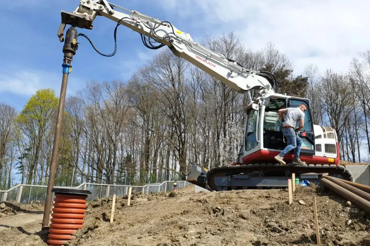 Graafmachine met hydraulische schroefmotor plaatst schroefpalen op een werf van Soiltek